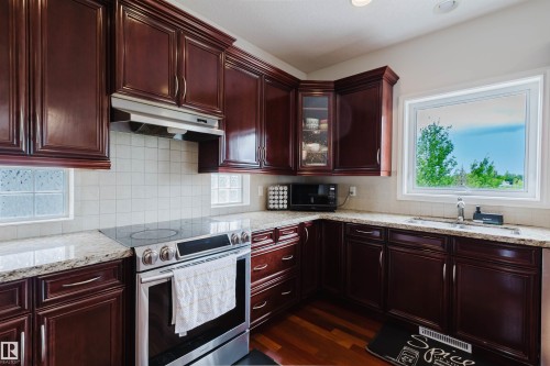 Kitchen featuring rich wood cabinetry, light-toned countertops, a stainless steel range with a ventilation hood, a double basin sink, and wood-finish flooring - 20524 58 Avenue, Edmonton, AB 