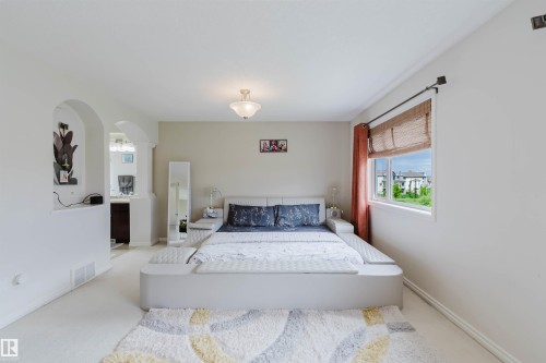 Carpeted room with a ceiling-mounted light fixture, a window with a curtain rod, and an arched entryway to an adjoining space featuring a dark wood-finish cabinet - 20524 58 Avenue, Edmonton, AB 