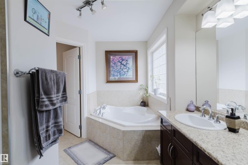 Bathroom featuring a corner soaking tub with tile surround, a single vanity with a light-colored countertop, dark wood-finish cabinetry, a white basin, and a mirrored wall - 20524 58 Avenue, Edmonton, AB 