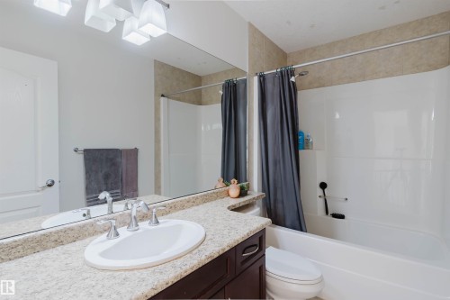 Bathroom featuring a built-in bathtub with shower, a vanity with an integrated sink, a light-colored countertop, and a large wall mirror - 20524 58 Avenue, Edmonton, AB 