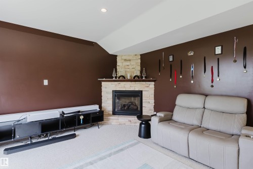 Cozy living area featuring a corner-stacked stone fireplace with a wood mantle, recessed lighting, and carpeting - 20524 58 Avenue, Edmonton, AB 