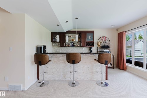 Built-in wet bar featuring dark wood cabinetry, a stone-finish countertop, and a textured stone-finish bar face - 20524 58 Avenue, Edmonton, AB 