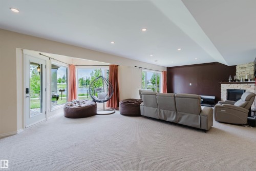 Spacious lower-level room featuring light-colored carpet, recessed lighting, and a stone-faced fireplace with a dark mantel - 20524 58 Avenue, Edmonton, AB 