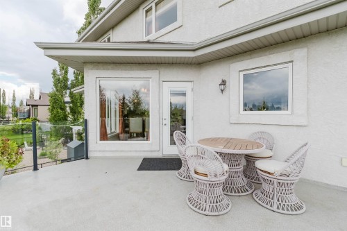 Expansive outdoor patio featuring a glass railing, large picture windows, a white paneled door, and a wall-mounted exterior light fixture - 20524 58 Avenue, Edmonton, AB 