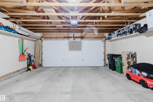 Attached garage with a white sectional door, exposed wood-frame ceiling, concrete flooring, overhead lighting, and built-in wall shelving - 20524 58 Avenue, Edmonton, AB 