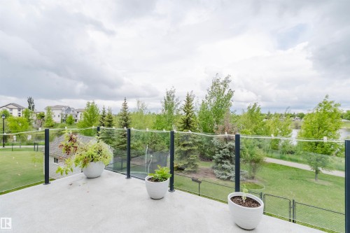 Exterior deck with glass railing, overlooking green spaces, mature trees, and residential structures in the background - 20524 58 Avenue, Edmonton, AB 