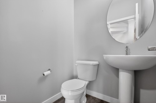 Pedestal sink with a modern oval mirror, chrome faucet, and wood-finish flooring - 90 1010 Rabbitt Hill Road Sw, Edmonton, AB - Indoor Photo Showing Bathroom