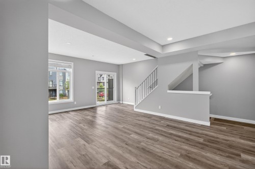 Spacious living area featuring wood-finish flooring, contemporary light gray walls, and recessed ceiling lighting - 90 1010 Rabbitt Hill Road Sw, Edmonton, AB - Indoor Photo Showing Other Room