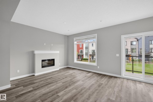 Living area featuring a built-in fireplace with a white mantel, wood-finish flooring, and light gray walls - 90 1010 Rabbitt Hill Road Sw, Edmonton, AB - Indoor Photo Showing Living Room With Fireplace