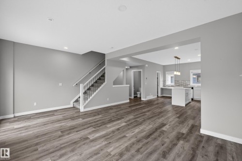 Open-concept living space featuring wood-finish flooring, recessed lighting, and a staircase with white risers and dark metal balusters - 90 1010 Rabbitt Hill Road Sw, Edmonton, AB - Indoor Photo Showing Kitchen