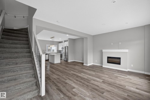 Spacious living area featuring wood-finish flooring and a contemporary fireplace with a white mantel - 90 1010 Rabbitt Hill Road Sw, Edmonton, AB - Indoor With Fireplace