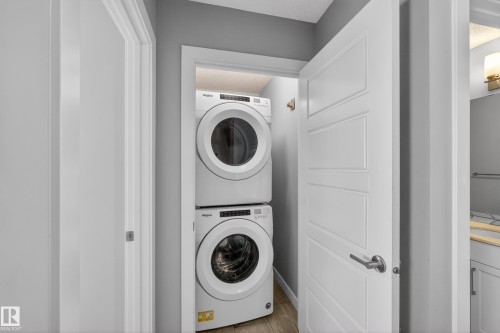Dedicated laundry closet featuring a stacked white washer and dryer, wood-finish flooring, white paneled door with brushed nickel hardware, and light gray wall paint - 90 1010 Rabbitt Hill Road Sw, Edmonton, AB - Indoor Photo Showing Laundry Room