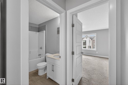 Full bathroom featuring a white vanity with a light-toned countertop, a tub/shower combination with tile surround, and wood-finish flooring - 90 1010 Rabbitt Hill Road Sw, Edmonton, AB - Indoor Photo Showing Bathroom