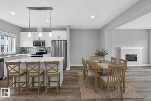 Modern kitchen featuring white cabinetry, stainless steel appliances, a large island with seating, and a decorative tile backsplash - 90 1010 Rabbitt Hill Road Sw, Edmonton, AB - Indoor Photo Showing Other Room