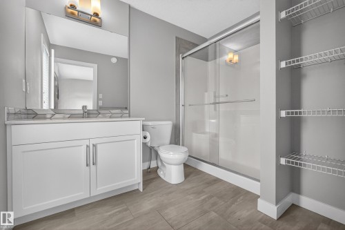 Contemporary bathroom featuring a white vanity with integrated sink, a full-width mirror with overhead lighting, a glass-enclosed shower, and wire shelving - 90 1010 Rabbitt Hill Road Sw, Edmonton, AB - Indoor Photo Showing Bathroom