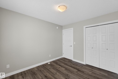 Interior room featuring light gray walls, wood-finish flooring, white baseboards, a flush-mount ceiling light, a white interior door with a silver handle, and bi-fold closet doors - 90 1010 Rabbitt Hill Road Sw, Edmonton, AB - Indoor Photo Showing Other Room
