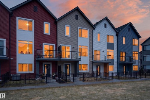 Contemporary townhome exteriors featuring varied siding colors, multiple balconies with glass railings, large windows, and a fenced front yard with a concrete walkway - 90 1010 Rabbitt Hill Road Sw, Edmonton, AB - Outdoor With Balcony With Facade