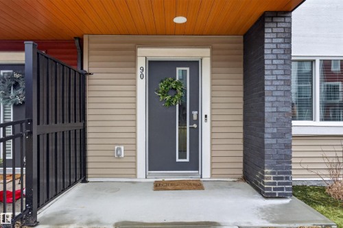 Inviting entry featuring a dark gray door with vertical window panels, set against horizontal tan siding - 90 1010 Rabbitt Hill Road Sw, Edmonton, AB - Outdoor With Exterior