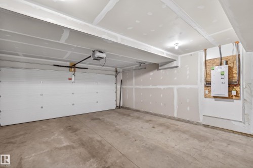 Spacious unfinished garage with an automatic overhead door, exposed drywall, concrete flooring, and a visible electrical panel - 90 1010 Rabbitt Hill Road Sw, Edmonton, AB - Indoor Photo Showing Garage