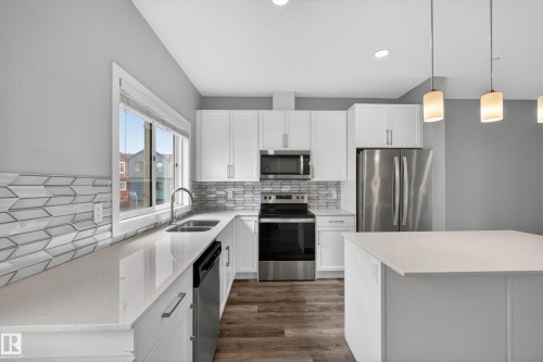 Contemporary kitchen featuring white cabinetry, light-toned countertops, stainless steel appliances, and wood-finish flooring - 90 1010 Rabbitt Hill Road Sw, Edmonton, AB - Indoor Photo Showing Kitchen With Stainless Steel Kitchen With Double Sink With Upgraded Kitchen