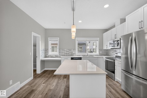 Kitchen featuring a central island with countertop, wood-finish flooring, stainless steel appliances, white cabinetry, and a patterned tile backsplash - 90 1010 Rabbitt Hill Road Sw, Edmonton, AB - Indoor Photo Showing Kitchen With Stainless Steel Kitchen With Upgraded Kitchen