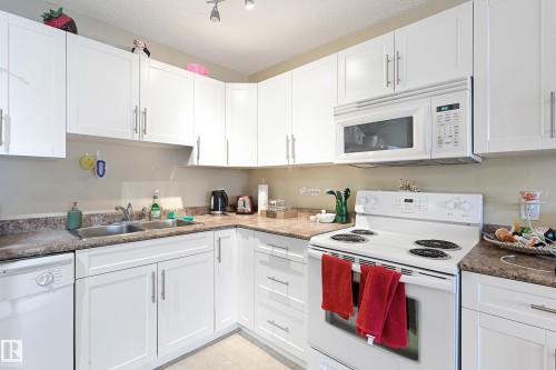 Well-appointed kitchen featuring abundant white cabinetry with brushed nickel hardware, laminate countertops, a double basin stainless steel sink, a white electric range, and a white over-the-range microwave - 901 9710 105 Street, Edmonton, AB - Indoor Photo Showing Kitchen With Double Sink