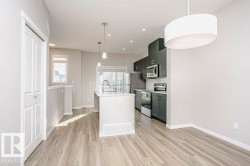 Open concept living area with light-toned flooring, featuring a modern kitchen with dark cabinetry and stainless steel appliances - 