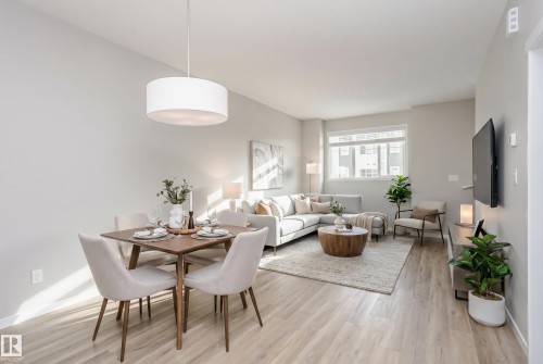 Open-concept living space featuring light wood-finish flooring, a contemporary drum pendant light, a large window, and neutral-toned walls - 320 Secord Boulevard, Edmonton, AB - Indoor