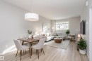 Open-concept living space featuring light wood-finish flooring, a contemporary drum pendant light, a large window, and neutral-toned walls - 320 Secord Boulevard, Edmonton, AB  - Indoor 
