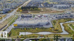 Aerial view showcasing the property's surrounding commercial buildings, a paved road with vehicles, and green spaces featuring ponds - 