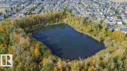Aerial view showcasing the surrounding neighborhood, featuring a body of water encircled by trees, and residential properties with varied roof colors - 