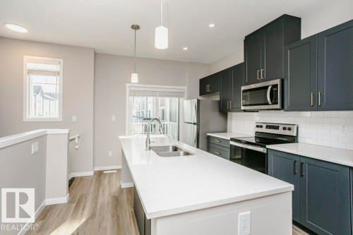Kitchen featuring an island with a double sink, stainless steel appliances, dark cabinetry, and white countertops - 320 Secord Boulevard, Edmonton, AB - Indoor Photo Showing Kitchen With Stainless Steel Kitchen With Double Sink With Upgraded Kitchen