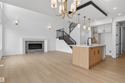 Open concept living space featuring high ceilings, wood-finish flooring, a linear fireplace with tile surround, a kitchen island with a white countertop and dark hardware, and a staircase with black railings - 