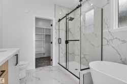 Modern bathroom featuring a freestanding soaking tub, a frameless glass shower enclosure with black hardware, and patterned floor and shower wall tile - 