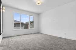 Bright, neutral-toned room featuring a large window, light gray carpeting, white baseboards, and a ceiling-mounted light fixture - 