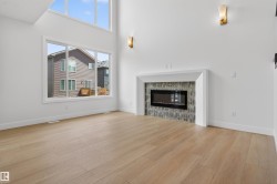 Expansive room featuring wood-finish flooring, a linear electric fireplace with a tiled surround, high ceilings, large windows, and contemporary wall sconces - 