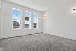 Spacious interior featuring a neutral color palette, three large windows, low-pile carpeting, white baseboards, and two wall-mounted sconces - 
