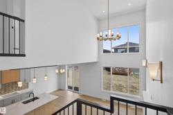 Open-concept living space featuring a two-story ceiling, large picture windows, wood-finish flooring, and a contemporary kitchen with light-toned cabinetry and a center island with sink - 