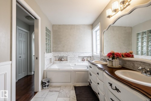 Bathroom featuring a built-in tub with marble tile surround and recessed shelving, dual vanity with undermount sinks, decorative mirror, and an overhead light fixture - 2036 Towne Centre Boulevard, Edmonton, AB - Indoor Photo Showing Bathroom