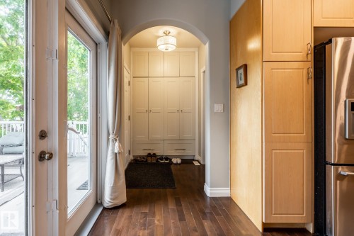 Hardwood flooring extends throughout this space featuring a built-in storage unit with archway, a glass-paneled door opening to an exterior deck with white railing, and wood-finish cabinetry - 2036 Towne Centre Boulevard, Edmonton, AB - Indoor Photo Showing Other Room