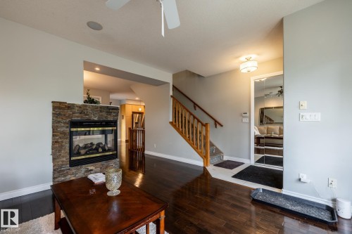 Living area featuring dark wood-finish flooring, a stone-clad fireplace with a black insert, and a staircase with wood railing - 2036 Towne Centre Boulevard, Edmonton, AB - Indoor Photo Showing Living Room With Fireplace