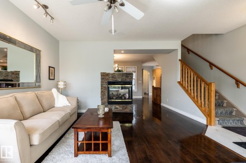 Spacious living area featuring dark wood-finish flooring, a stone-clad fireplace, and a ceiling fan with integrated lighting - 2036 Towne Centre Boulevard, Edmonton, AB - Indoor Photo Showing Living Room With Fireplace