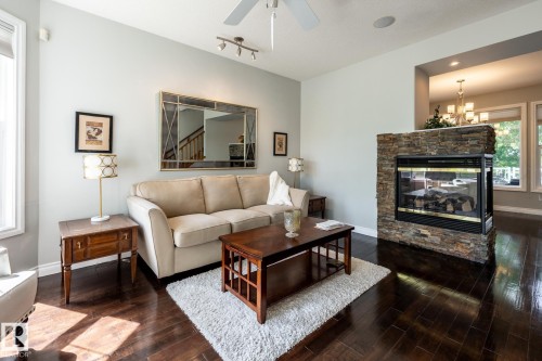 Living area featuring wood-finish flooring, a stone-wrapped fireplace, and light-toned walls - 2036 Towne Centre Boulevard, Edmonton, AB - Indoor Photo Showing Living Room With Fireplace