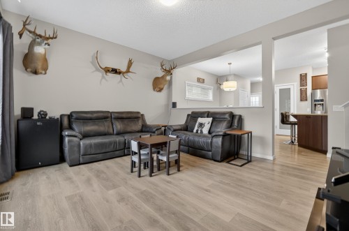 Living area featuring light wood-finish flooring, neutral wall tones, and a partial wall opening to the kitchen - 70 James Crescent, St. Albert, AB 