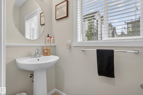Pedestal sink with chrome faucet, circular wall mirror, and window with horizontal blinds - 70 James Crescent, St. Albert, AB 
