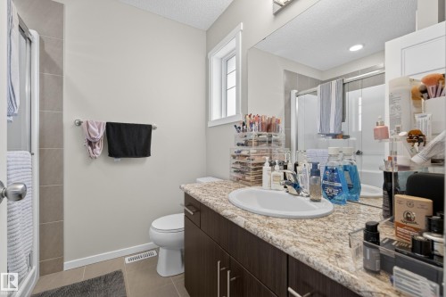 Bathroom featuring a single vanity with an integrated sink, a speckled countertop, dark wood-finish cabinetry, a mirror, and a window - 70 James Crescent, St. Albert, AB 