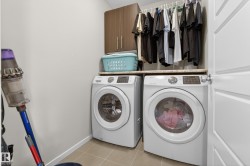 Dedicated laundry area featuring front-loading washer and dryer units, a light-toned countertop, and overhead cabinetry - 