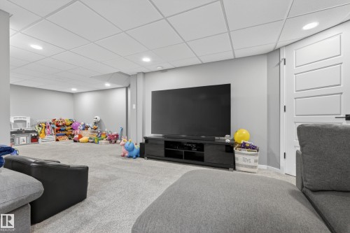 Spacious carpeted room featuring a white paneled door, flush-mounted ceiling lights, a drop ceiling, and light gray wall paint - 70 James Crescent, St. Albert, AB 