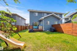 Spacious backyard featuring a wooden privacy fence, a wooden deck, and a multi-story residence with blue siding - 