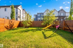 Fenced backyard featuring mature trees, a wooden swing set with slide, and a groomed lawn - 
